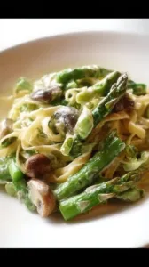 Grüner Spargel mit Pilzen auf Bandnudeln auf einem Teller angerichtet