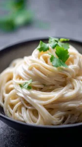 Pasta mit Cashew-Käse-Sauce auf einem Teller, garniert mit frischen Kräutern.