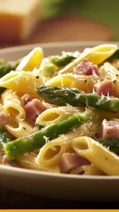 Pasta mit Schinken, Spargel und Parmesan auf einem Teller angerichtet.